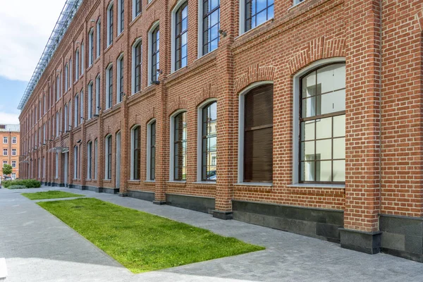 Office building in loft style. Large Windows. Red brick wall. Grass in front of the building