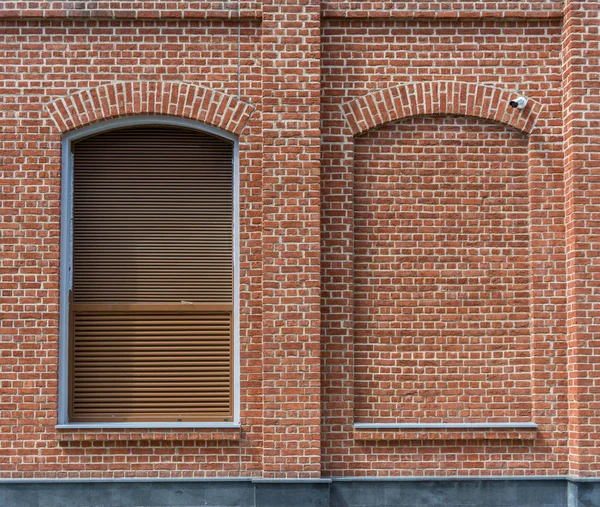 The building is made of brick in loft style. Window with blinds and a window laid with brick. Facade of house.
