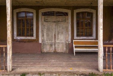 Eski ahşap evin girişinde, verandada eski kanepe var. Büyük kapı.