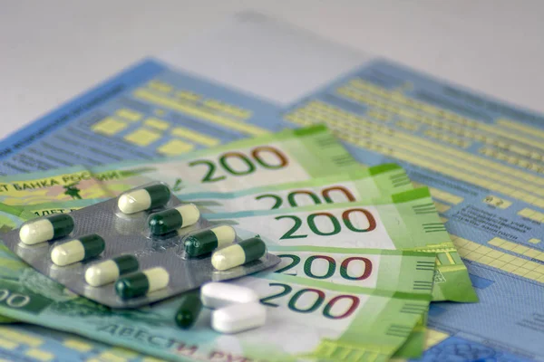Russia. Russian sick leave with seals. The bottle of pills and a few pills in bulk. Russian money-banknotes of 200 rubles. Focus on the nearest pills.