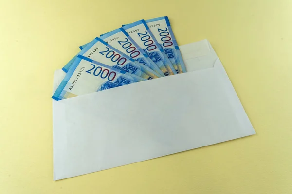 Russian cash in white envelope on yellow background. Banknotes 2000 rubles