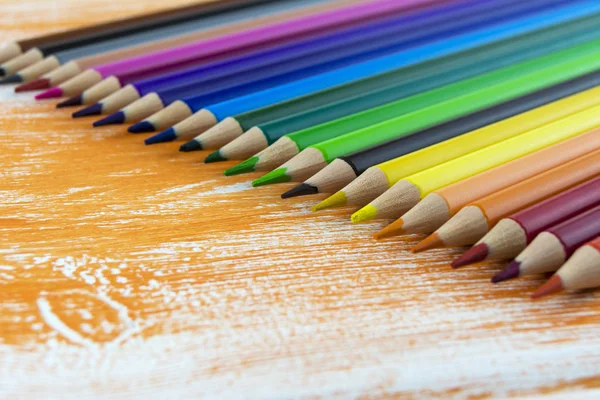 Muchos lápices de colores que yacen en un tablero naranja —  Fotos de Stock