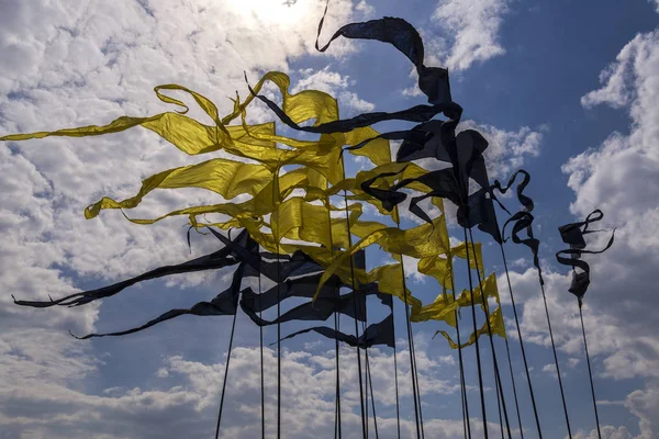 Many flags on the flagpoles of yellow and black colors. Flags in the form of narrow triangles