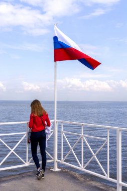 Peterhof, Rusya, 08 Ağustos 2019. Yalnız bir kız Rus bayrağı ile bayrak direğinde deniz iskelesi üzerinde duruyor.