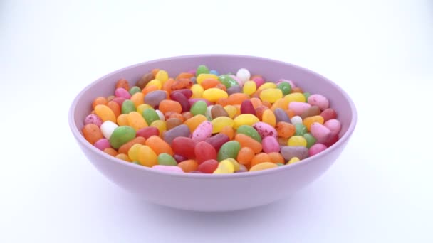 Stapel kleine boon vormige suiker jelly snoepjes. Roterende in paarse kom op tafel zet. Geïsoleerd. — Stockvideo
