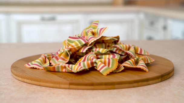 Makro zbliżenie sterty farfalle arcobaleno (rainbow muszki) makaronu na talerzu. Obracanie kamery z białą kuchnię na tle. Dolly strzał. — Wideo stockowe