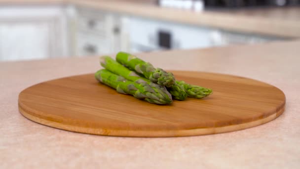 Opslagruimte voor verse groene asperges op de plaat. Draaiende camera met witte keuken op de achtergrond. Dolly-shot. — Stockvideo