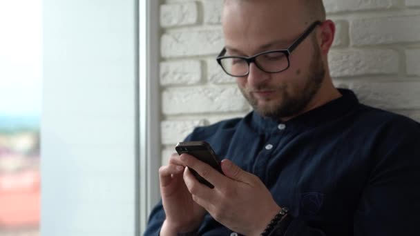 Молодой Человек Сидит Окна Пролистывает Экран Своего Мобильного Телефона Закрывай — стоковое видео