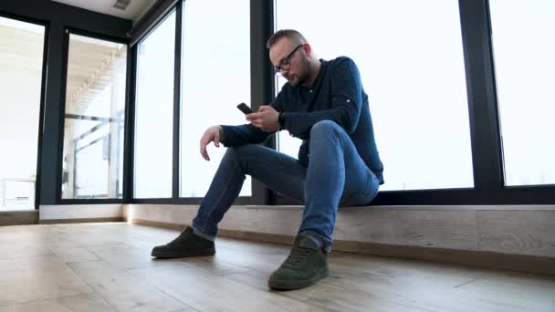 Joven Está Sentado Cerca Ventana Panorámica Gira Través Pantalla Teléfono — Vídeos de Stock