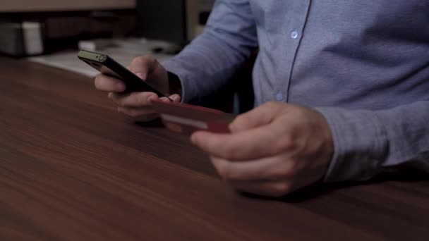 Geschäftsmann hält Handy in der einen Hand und Kreditkarte in der anderen. Er benutzt seine Kreditkarte, um online zu bezahlen. Video mit Schiebereglern. — Stockvideo