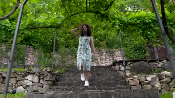 Souriante fille asiatique dans la robe d'été descend les escaliers dans le parc. promenades le long de la vigne — Video