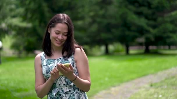 Happy looking asian woman walks in the park and chatting in social networks. — Stock Video