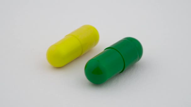 Dos cápsulas duras de almidón girando sobre la mesa giratoria. Color amarillo y verde. Aislado sobre fondo blanco. Primer plano macro . — Vídeos de Stock