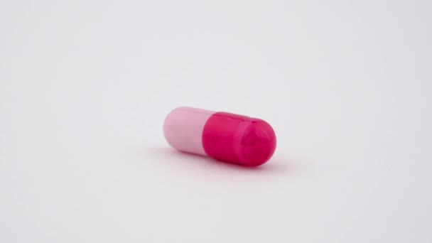 One hard starch capsule rotates on the turn table. Red and pink color. Isolated on white background. Close up macro. — Stock Video