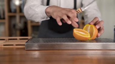 Closeup barmen eller kesim çubuğunda turuncu meyve karşı daha önce yapımı bir kokteyl içinde.