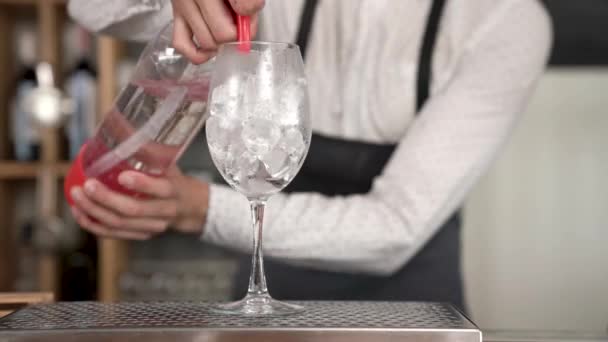 一个英俊的年轻酒保从苏打虹吸里倒出一层波光粼粼的水, 然后用冰块把杯子倒入玻璃杯中。酒吧柜台。特写. — 图库视频影像