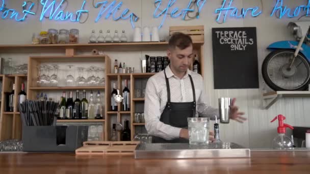 Camarero Flair. Un apuesto camarero joven vierte un licor de curazao azul en un vaso con cubitos de hielo . — Vídeos de Stock