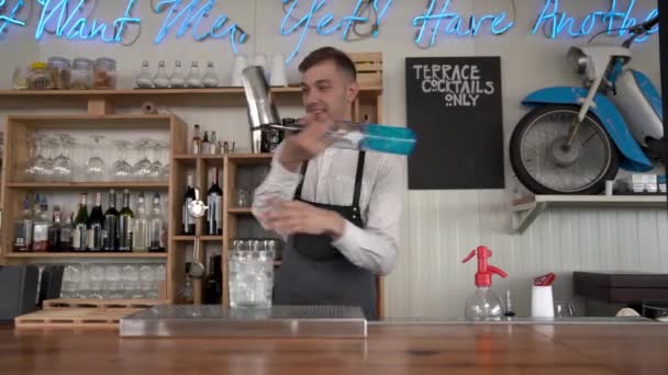 Funny, smiling bartender pours a blue curacao liquor into a glass with ice cubes. Flair bartending. — Stock Video