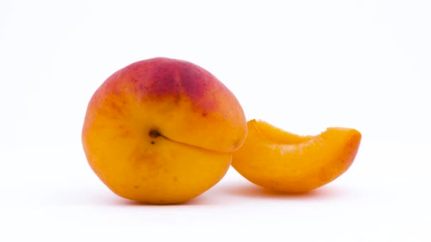 One whole and one slice of apricot fruit. Rotating on the turntable. Isolated on the white background. Close up. Macro. — Stock Video