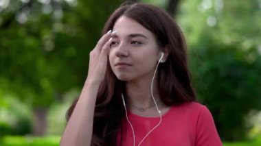 Bir close-up kulaklık giyen ve uyum içinde hareket genç ve güzel bir kadın. Doğada dışarıda bekliyor.