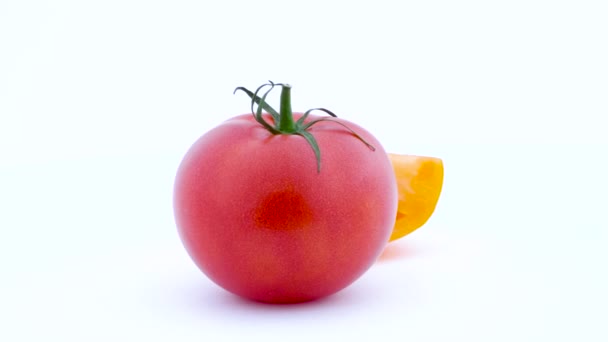 En hel stor röd tomat och en del av gul tomat. Långsamt roterande på skivtallriken. Isolerad på den vita bakgrunden. Vänstra halvan av ramen. Närbild. Makro. — Stockvideo