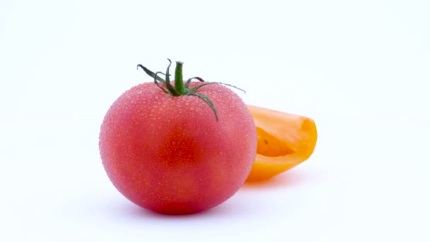 Eine ganze große rote Tomate und eine halbe gelbe Tomate mit Wassertropfen. sich langsam auf der Drehscheibe drehend. isoliert auf weißem Hintergrund. linke Hälfte des Rahmens. Nahaufnahme. Makro. — Stockvideo
