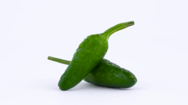 Makro-fotografering av två små gröna piri-piri chili paprika med vatten droppar. Roterande på skivtallriken. Isolerad på den vita bakgrunden. — Stockvideo