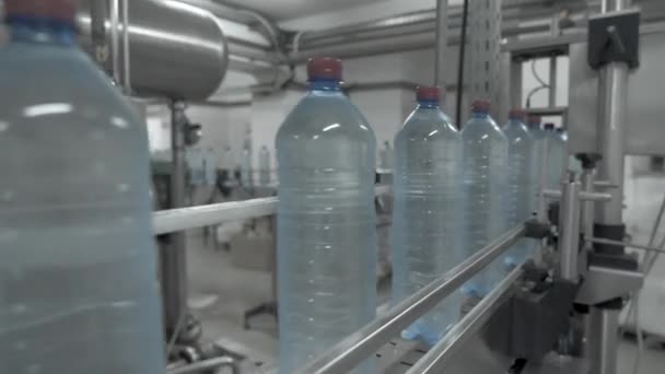 Grote blauwe plastic flessen gevuld met transparante vloeistof op de automatische transportband regel. Close-up van water bottelen lijn. — Stockvideo