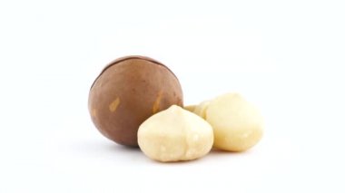 İki tam ve yarım macadamia nut çekirdekleri ve bir somun inshelled. Beyaz arka plan üzerinde izole pikap üzerinde yavaş yavaş döner. Yakın çekim. Makro.