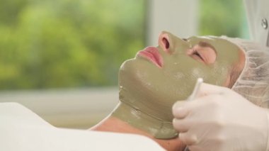 Kadının yüzüne yeşil maske ile görünümünü yakından. Bir beyaz lastik eldiven elinde daha fazla maskesi altında çene ve boyun uygular