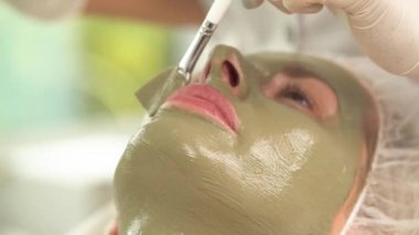 Kadının yüzüne yeşil maske ile görünümünü yakından. Bir el bir fırça ile üst dudak üzerinde burun altında daha fazla maskesi uygular