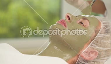 Kadının yüzüne yeşil maske ile görünümünü yakından. Bir beyaz lastik eldiven elinde daha fazla maskesi alnında uygular.