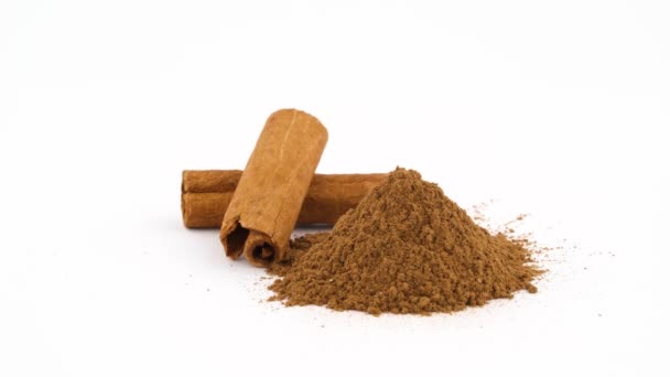 Two cinnamon sticks and heap of ground cinnamon powder. Rotating on the turntable. Isolated on the white background. Close-up. Macro. — Stock Video