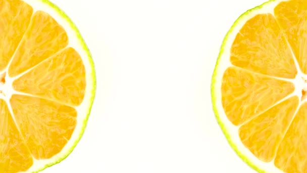 Duas seções transversais de uma tangerina verde estão girando em dois cantos do quadro. Isolado no fundo branco. Close-up. Macro . — Vídeo de Stock