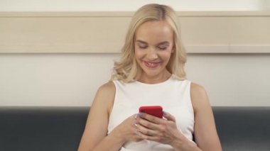 A kadar yakın bir güzel sarışın koltukta oturmaktan seyir telefon gülümseyen. Kamera soldan sağa taşır..