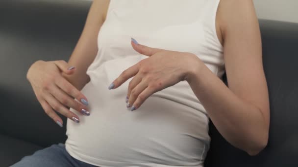 A på nära håll av en gravid mage rörd av kvinnas händer. Kameran flyttas sakta botten. Kvinnan ler, ser framför henne och sedan ner igen. — Stockvideo