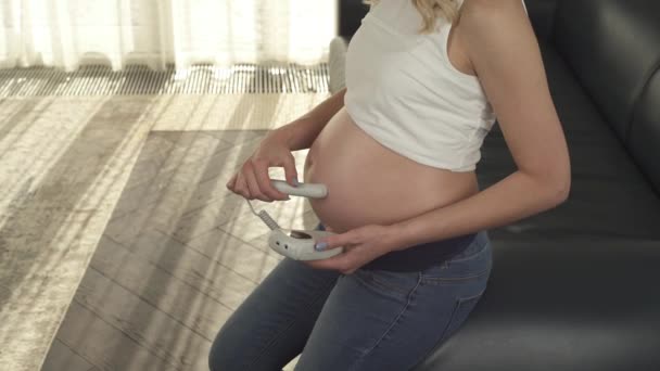 En sidovy av en gravid kvinnas mage. Hon kontrollerar barnets hjärtslag står i rummet. Kameran flyttas botten. Kvinnan slutar nästan i en punkt och ler, tittar på magen. — Stockvideo