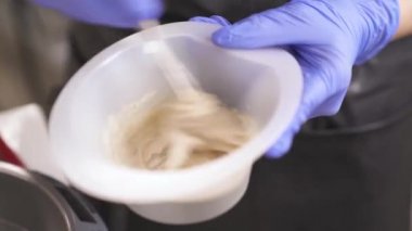 A yakın çekim el saç boyaları ile bir kase tutarak ve bu çevrelerde, saat yönünün tersine önce daha sonra saat yönünde çırpma mavi kauçuk eldiven