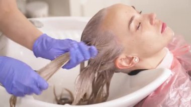 Üstten görünüm boyalı saç kafasını geri yıkama havzasında tutan sarışın. Kuaför ıslak saç tellerinin uzunluğuna uzanır.