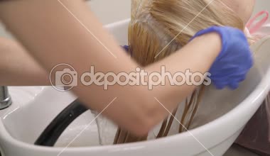 A yakın çekim sarışın saç geri yıkama havzasında Kuaför tarafından yıkanmış boyalı. O bir duş tutar ve saç durulama.