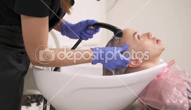 Yan görünümü kafa lavabo içinde ayak bağı sarışın kadar yakın. Kuaför duş tutar ve saç yıkar. Sarışın bir anlamı.