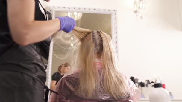 Un primo piano di un parrucchiere in piedi alla sinistra della bionda e prendendo fili tinti uno per uno. La vista in basso . — Video Stock