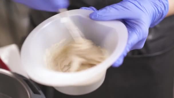 A close up of hands in blue rubber gloves holding a bowl with hair-dye and whisking it in circles, anticlockwise first, then clockwise — Stock Video