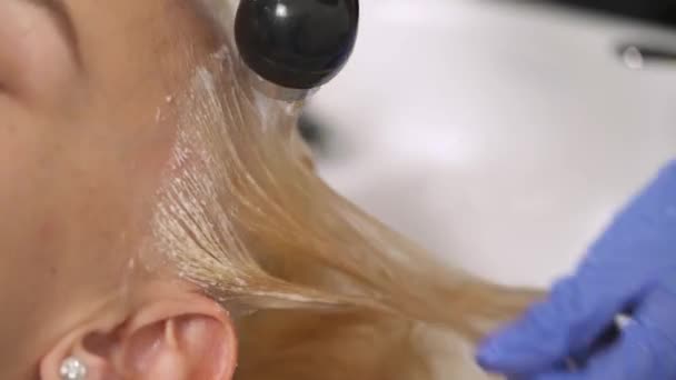 Un primer plano de una mano en un guante de goma azul lavando el pelo teñido de la rubia en el lavabo. El cabello se lava y se enjuaga de la ducha — Vídeo de stock