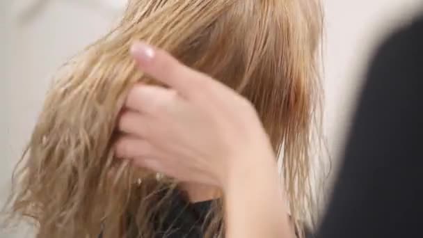 Zblízka pohled na mokré blond barvené vlasy. Kadeřnictví ruka táhne to, dává trochu třást a začne sušení s vysoušečem na délku vlasů. Kamera se pohybuje sledovat pohyb shora dolů. — Stock video