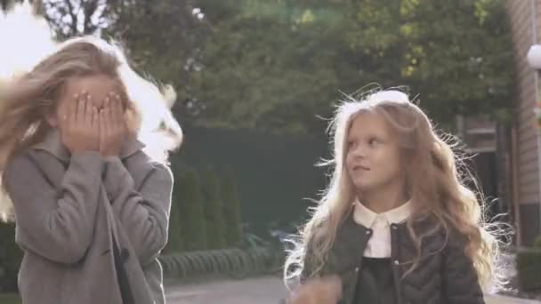 两个漂亮的金发女孩扔头发 玩偷看 并调整头发在风中 大一点的女孩背对着镜头 整理年轻女孩的头发 — 图库视频影像