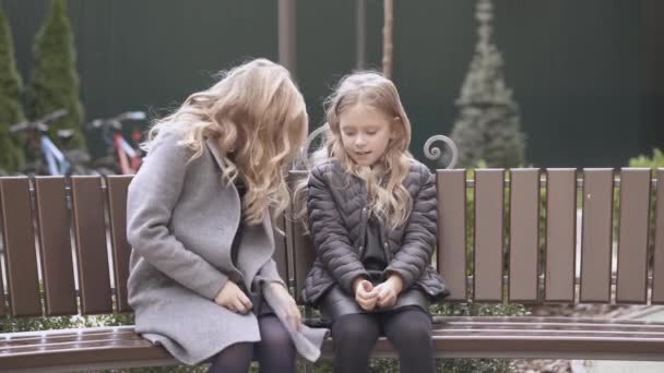 Auf Der Bank Sitzt Ein Niedliches Blondes Kleines Mädchen Schwarzer — Stockvideo