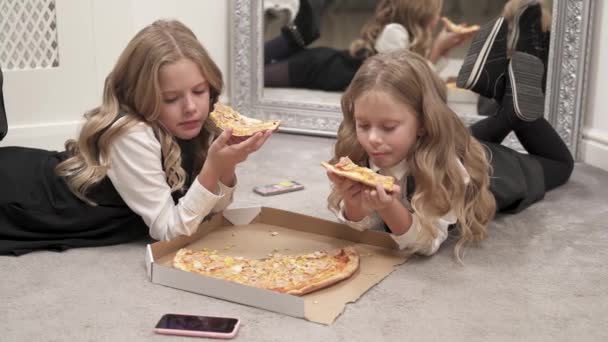 两个漂亮的金发女孩躺在地板上吃披萨 有一个打开的盒子 前面有比萨饼 他们看着手机屏幕 — 图库视频影像