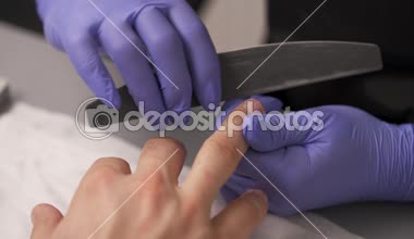 Menekşe eldiven elinde manikürcü Close-up bir tırnak törpüsü kullanarak bir adam tırnakları şekillendirme tamamlandıktan.