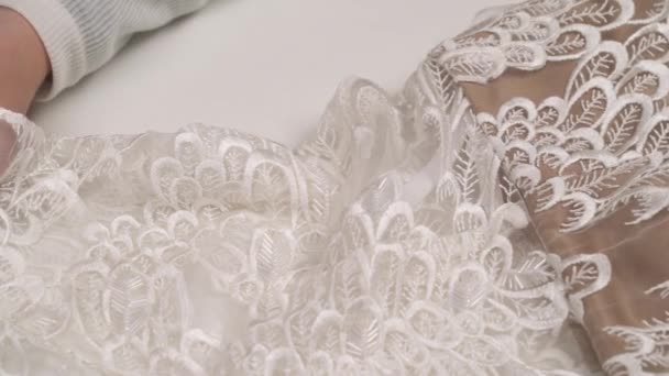 A close-up of ornamented fabric lying on the table and woman's hands stitching the hem of the lace — Stock Video